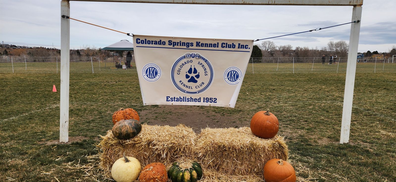 The Colorado Springs Kennel Club banner, reading Established 1952, above hay bales and pumpkins at the club Fast CAT